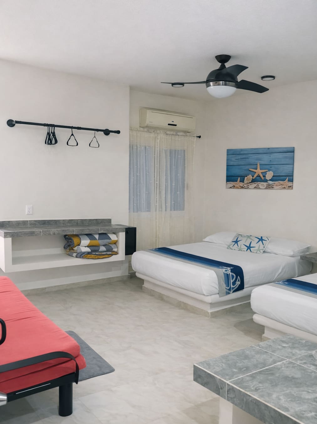 Vista de una de las camas dobles, Aire Acondicionado, ventilador, sofá cama, área para acomodar ropa,  decoración y buró de la habitación Triple 4 – Casa Tania