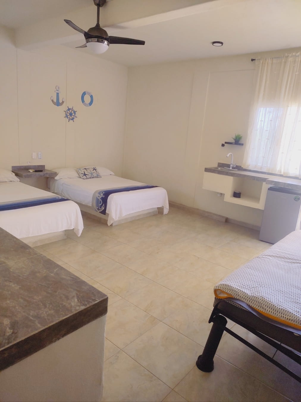 Vista de las camas dobles, Aire Acondicionado, ventilador, sofá cama, área para acomodar ropa,  decoración y buró de la habitación Triple 4 – Casa Tania